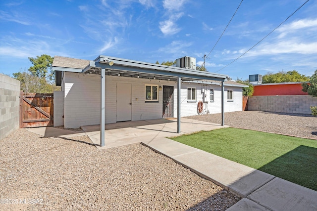 rear view of house featuring a gate, concrete block siding, fence, and central AC