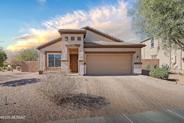 view of front of home featuring an attached garage, fence, decorative driveway, and stucco siding