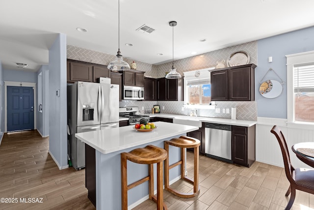 kitchen with stainless steel appliances, dark brown cabinets, light countertops, and visible vents