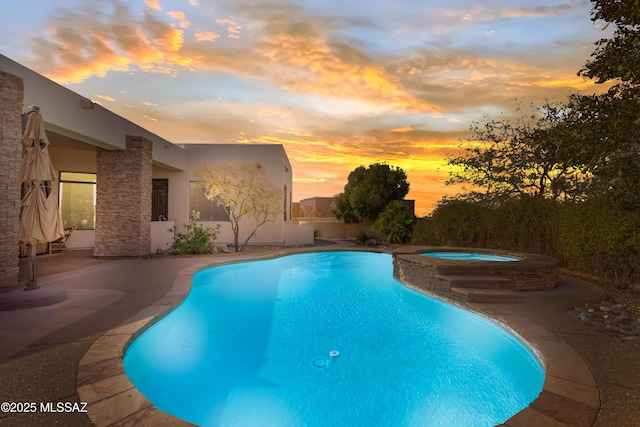 pool at dusk featuring a pool with connected hot tub and a patio area