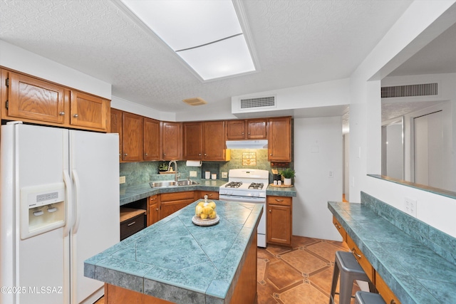 kitchen featuring tasteful backsplash, visible vents, brown cabinetry, white appliances, and a sink