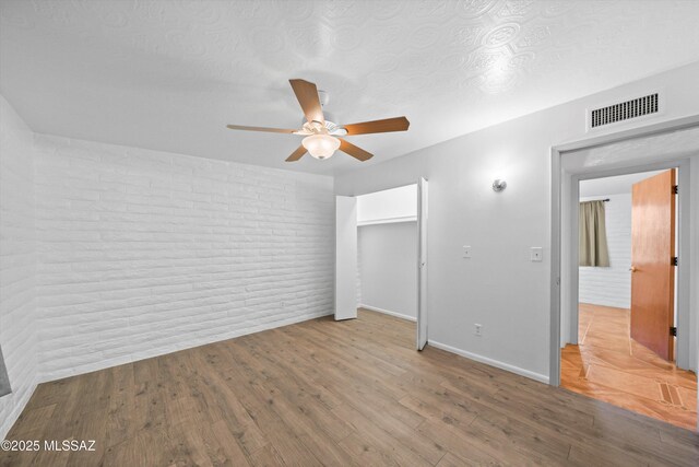 unfurnished bedroom with visible vents, a textured ceiling, wood finished floors, brick wall, and baseboards