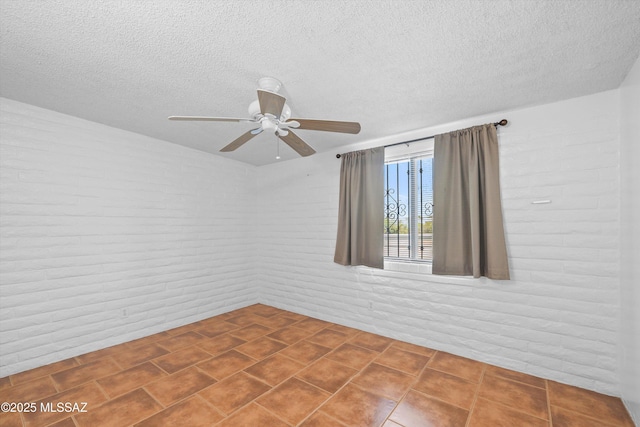 empty room featuring tile patterned floors, brick wall, a textured ceiling, and a ceiling fan