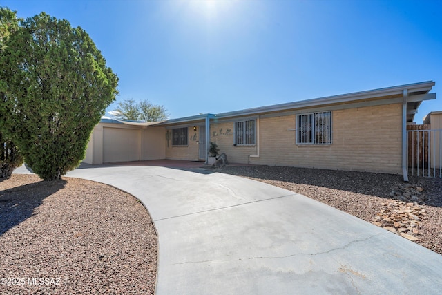 ranch-style home with driveway, brick siding, an attached garage, and fence