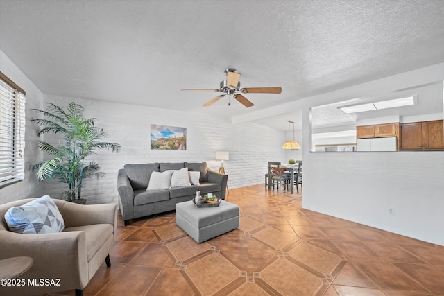 living area featuring ceiling fan, tile patterned floors, brick wall, and a textured ceiling