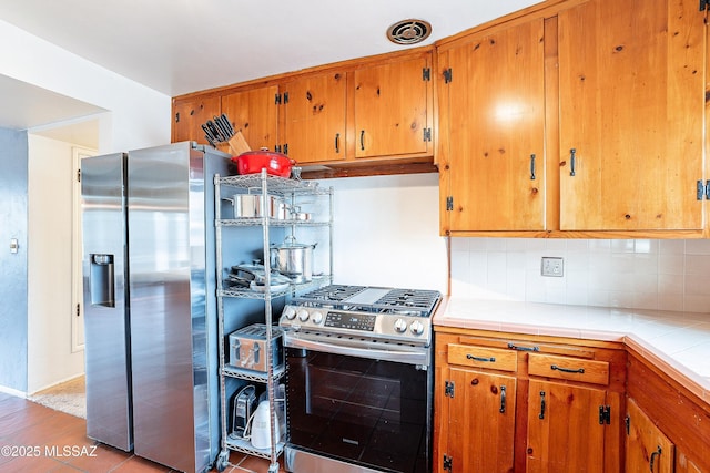 kitchen with stainless steel appliances, brown cabinets, backsplash, and tile countertops