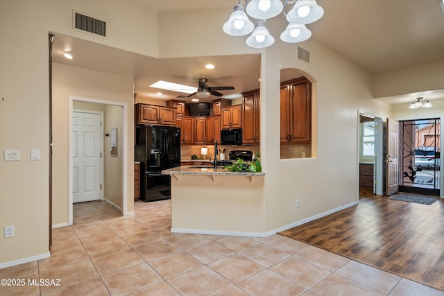 kitchen with visible vents, light tile patterned floors, a peninsula, arched walkways, and black appliances