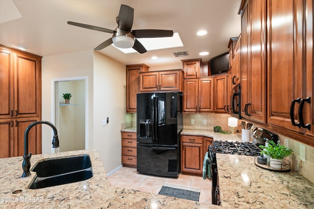 kitchen with light stone countertops, a sink, decorative backsplash, black appliances, and brown cabinets
