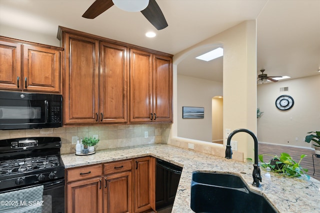 kitchen with backsplash, light stone counters, black appliances, a ceiling fan, and a sink