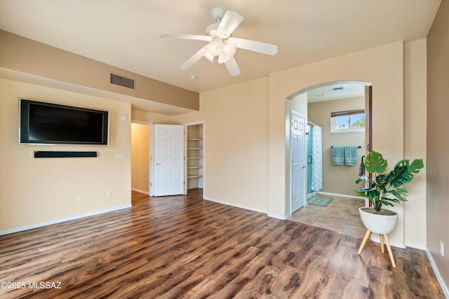 unfurnished living room featuring wood finished floors, visible vents, baseboards, arched walkways, and ceiling fan