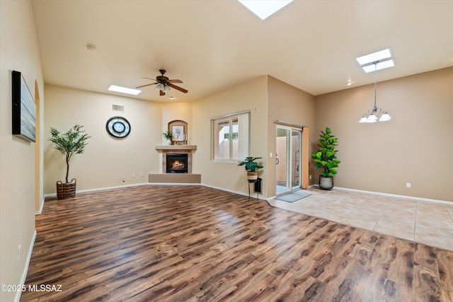 foyer entrance with ceiling fan with notable chandelier, a warm lit fireplace, wood finished floors, a skylight, and baseboards