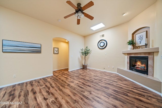 unfurnished living room featuring ceiling fan, vaulted ceiling, a tile fireplace, wood finished floors, and arched walkways