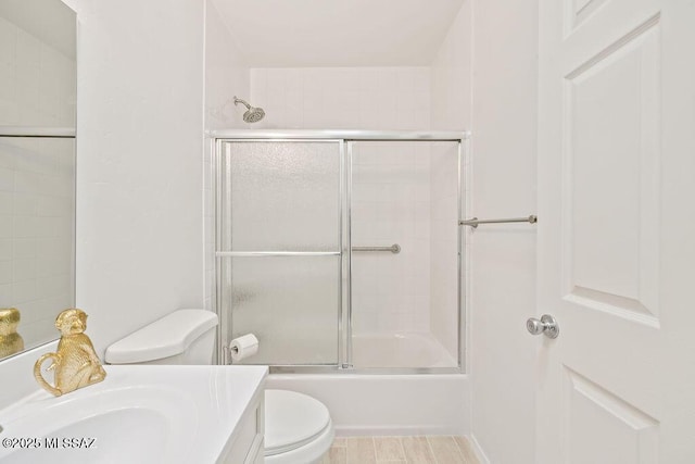 bathroom with vanity, shower / bath combination with glass door, wood finished floors, and toilet