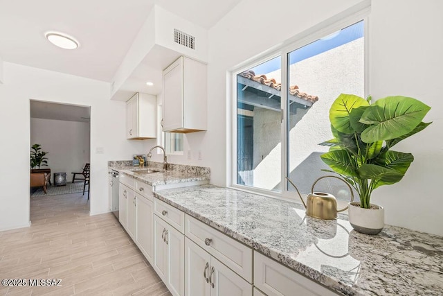 kitchen with light wood-style flooring, a sink, visible vents, white cabinetry, and light stone countertops