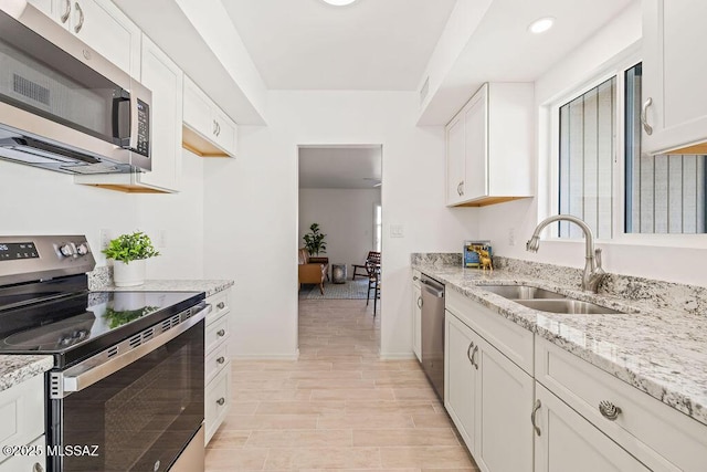 kitchen with light stone counters, appliances with stainless steel finishes, a sink, and white cabinetry