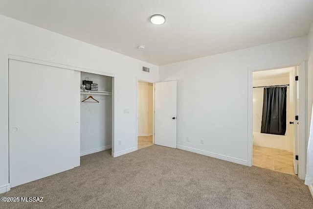 unfurnished bedroom featuring carpet, a closet, visible vents, and ensuite bath