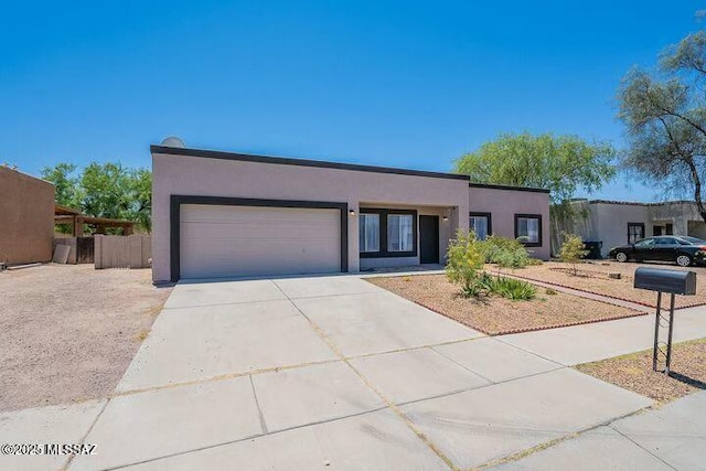 pueblo revival-style home with an attached garage, concrete driveway, and stucco siding