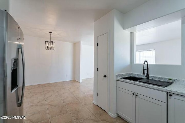 kitchen with stainless steel fridge with ice dispenser, hanging light fixtures, light stone countertops, white cabinetry, and a sink