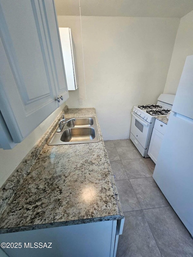 kitchen with light tile patterned floors, white appliances, a sink, white cabinets, and dark countertops