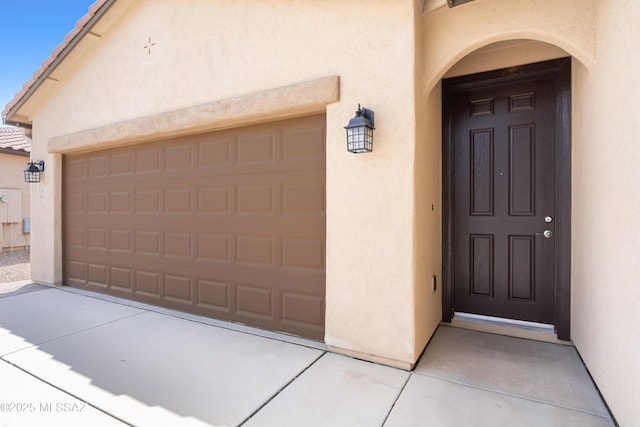 entrance to property with a garage, a tile roof, and stucco siding