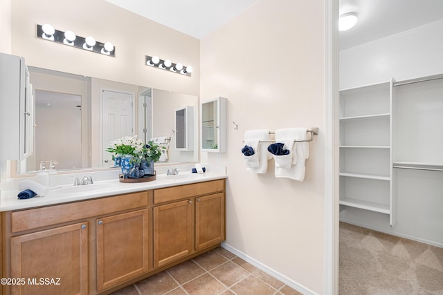 full bathroom featuring a spacious closet, double vanity, a sink, and baseboards
