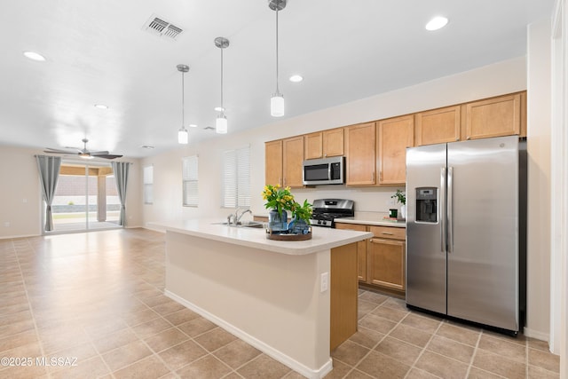 kitchen with stainless steel appliances, light countertops, hanging light fixtures, a sink, and an island with sink