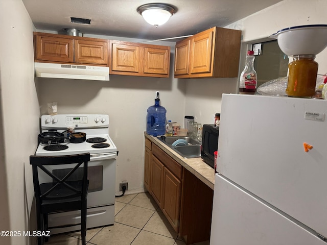 kitchen featuring light tile patterned floors, light countertops, brown cabinetry, white appliances, and under cabinet range hood