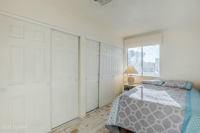 bedroom featuring light wood-type flooring, visible vents, and multiple closets