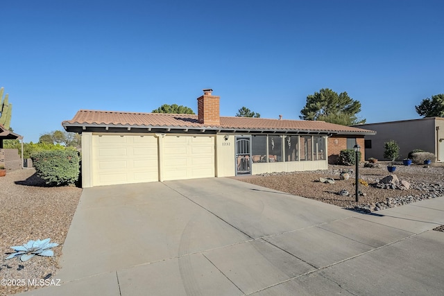 ranch-style house featuring a chimney, a tiled roof, an attached garage, and concrete driveway