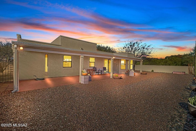 back of house at dusk with a patio and stucco siding