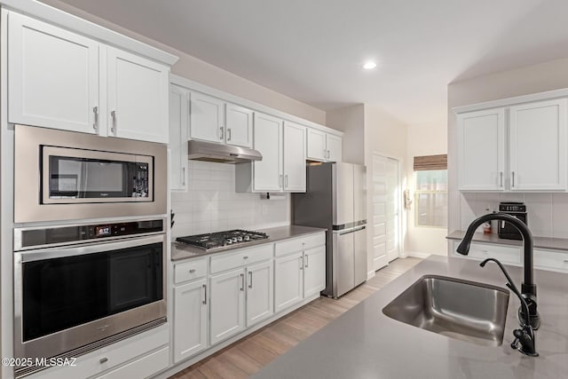 kitchen with tasteful backsplash, white cabinets, appliances with stainless steel finishes, under cabinet range hood, and a sink