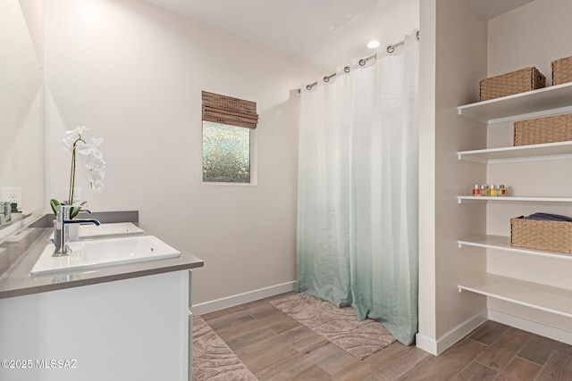 full bath featuring double vanity, wood tiled floor, a sink, a shower with curtain, and baseboards