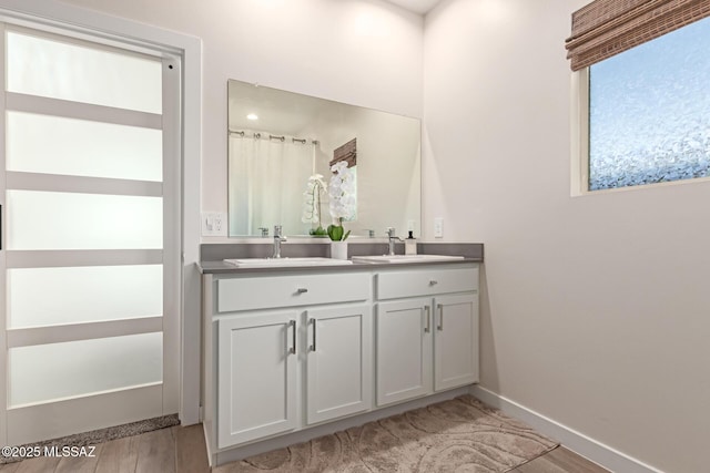 bathroom with double vanity, wood finished floors, a sink, and baseboards