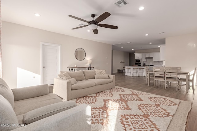 living room with ceiling fan, visible vents, wood finished floors, and recessed lighting