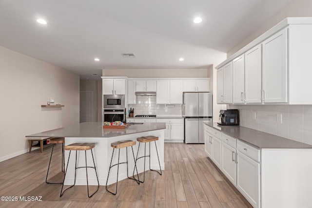 kitchen featuring white cabinets, light wood finished floors, stainless steel appliances, and a kitchen breakfast bar