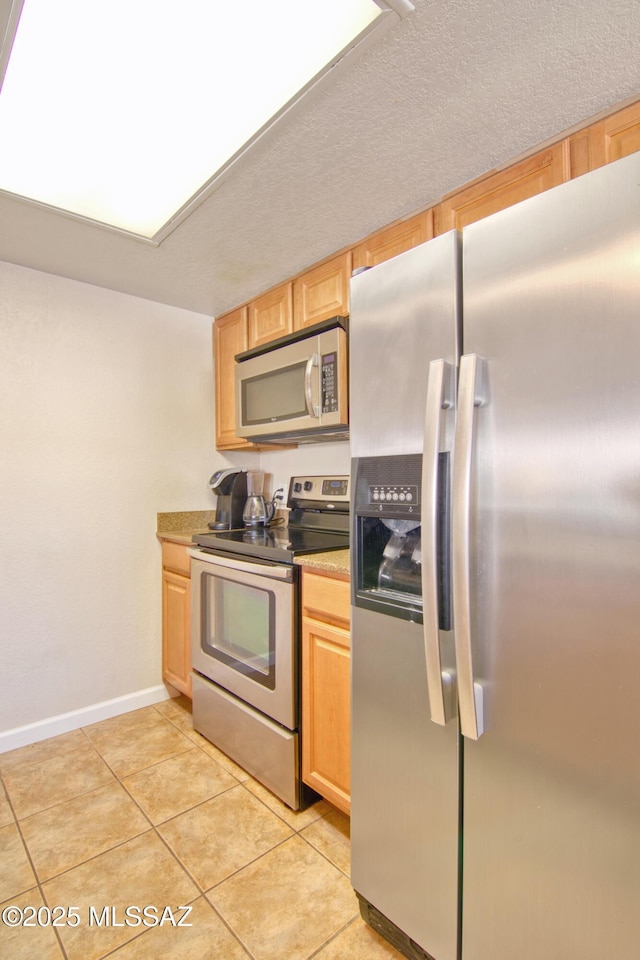 kitchen featuring light tile patterned floors, a textured ceiling, baseboards, appliances with stainless steel finishes, and light brown cabinetry