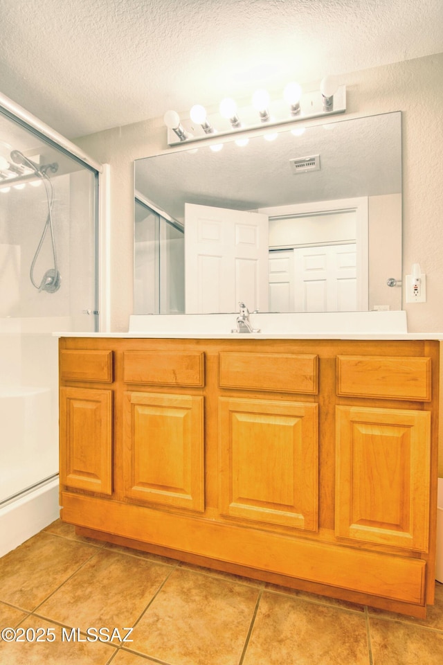 full bath featuring a stall shower, vanity, a textured ceiling, tile patterned flooring, and visible vents