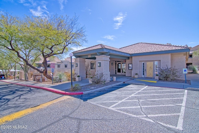 view of front facade featuring uncovered parking, stucco siding, a tiled roof, and french doors