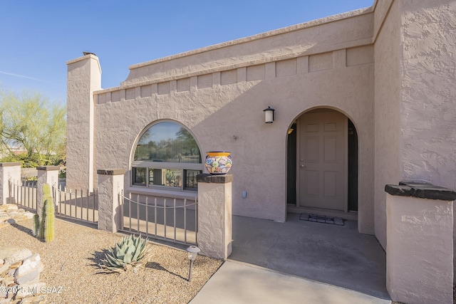 doorway to property featuring a chimney, fence, and stucco siding