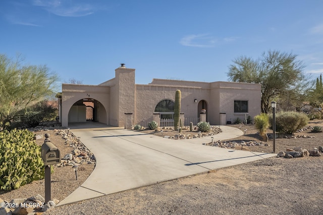 southwest-style home featuring concrete driveway, a chimney, and stucco siding