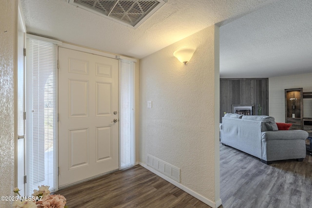 foyer featuring a textured ceiling, a textured wall, wood finished floors, and visible vents