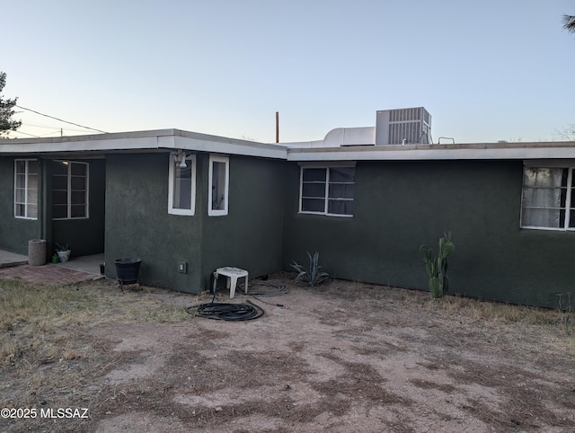 back of house with stucco siding and central air condition unit