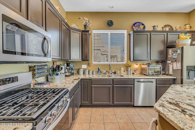 kitchen featuring appliances with stainless steel finishes, a sink, light stone counters, and dark brown cabinetry
