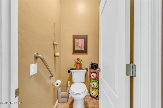 bathroom featuring a textured wall, tile patterned flooring, toilet, and baseboards