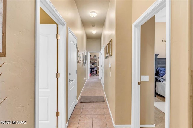 hall with a textured wall, baseboards, and light tile patterned floors