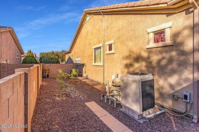 view of property exterior with stucco siding, a fenced backyard, a tile roof, and central air condition unit