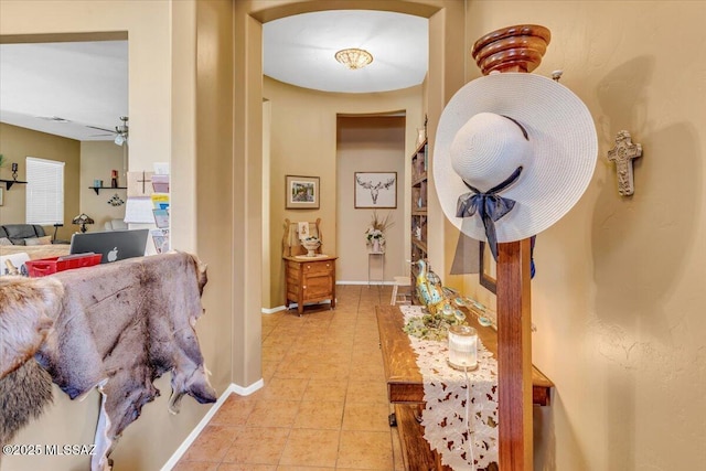 hallway featuring arched walkways, baseboards, and light tile patterned floors