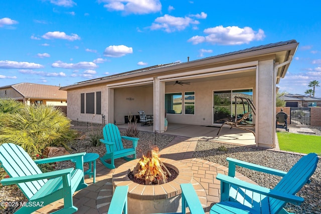 back of house featuring stucco siding, a ceiling fan, fence, a fire pit, and a patio area