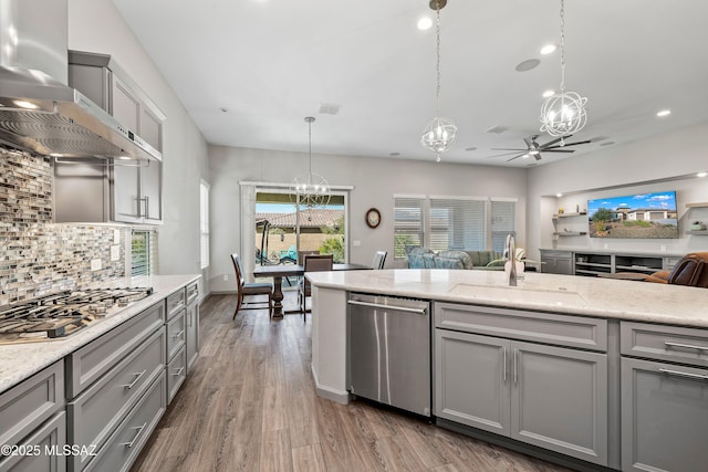 kitchen with open floor plan, appliances with stainless steel finishes, gray cabinetry, and wall chimney range hood