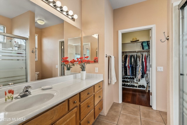 full bath featuring a stall shower, toilet, tile patterned floors, a walk in closet, and vanity